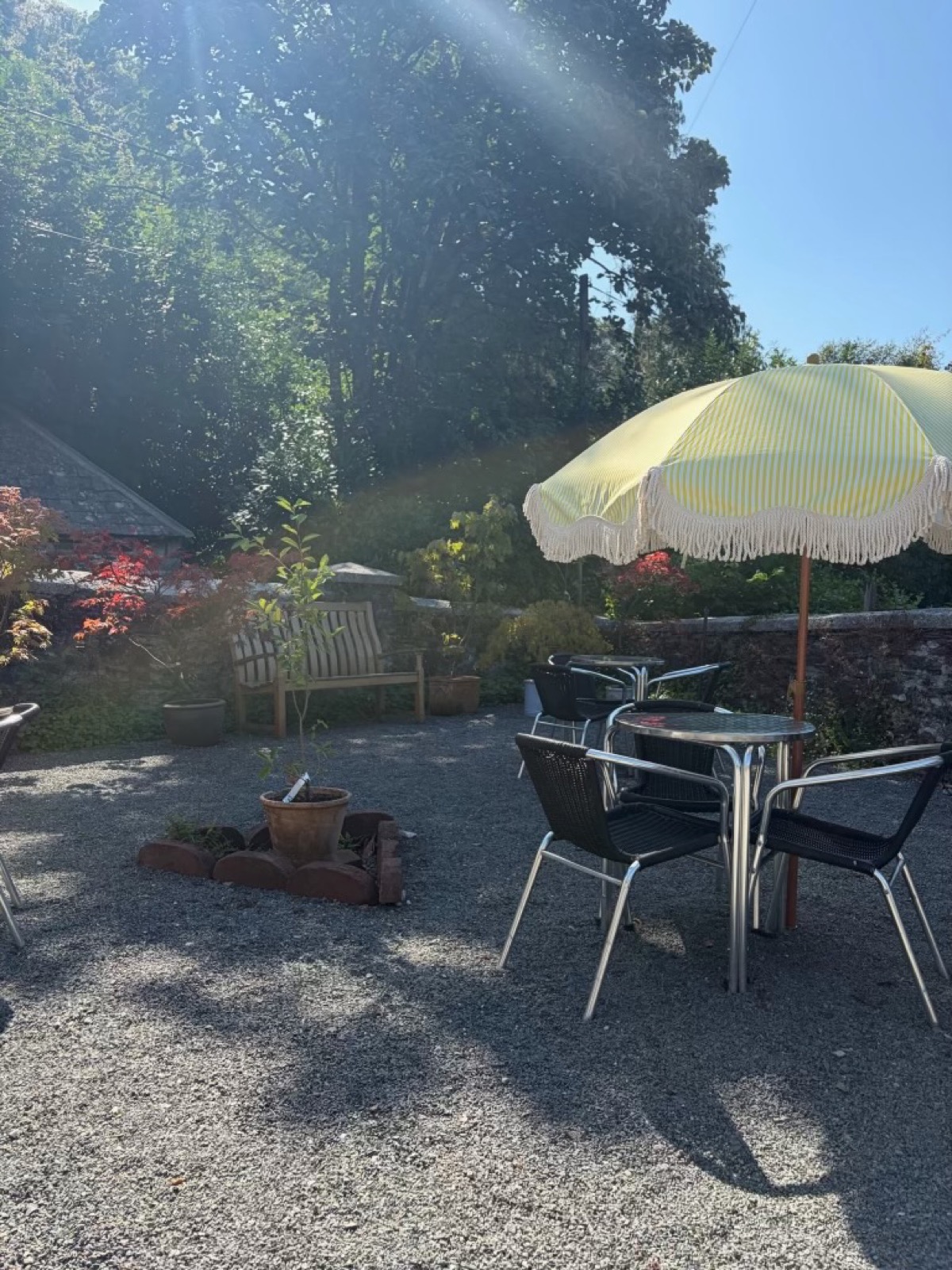 Tables and chairs outside the small cafe, with a parasol and garden views