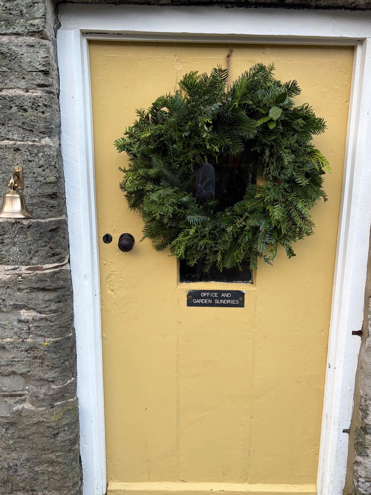 An evergreen Christmas wreath on the yellow garden shop door